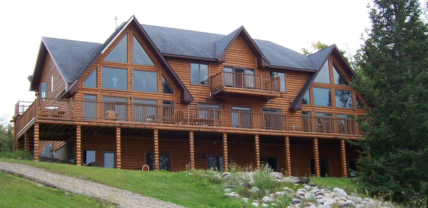 a log lodge with a large wrap-around deck on the second level and patio on the ground level